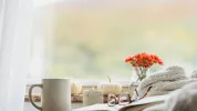 уютный интерьерный снимок книги и одеяла на стуле или диване, рядом с кружкой чая / кофе